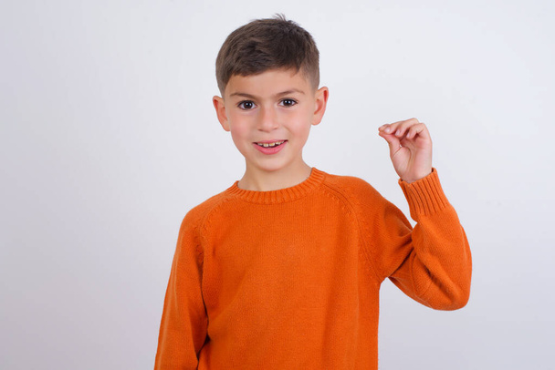 Caucasian kid boy wearing knitted orange sweater standing over white background pointing up with hand showing up seven fingers gesture in Chinese sign language Q. - Fotografie, Obrázek