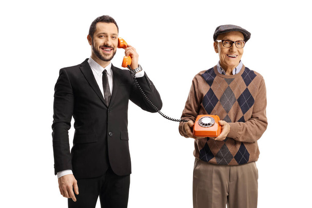 Elderly man holding a vintage rotary phone and a young man talking isolated on white background - Foto, imagen
