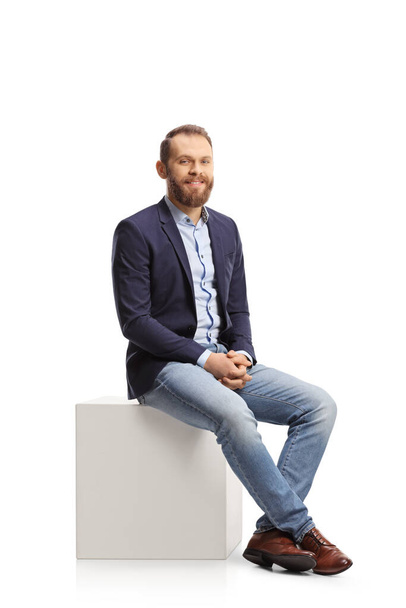 Young professional man sitting on a white cube and smiling isolated on white background - Foto, immagini