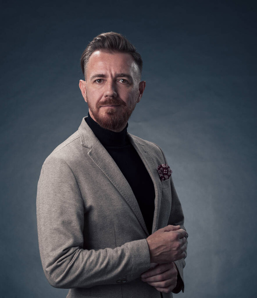Portrait of a stylish elegant senior businessman with a beard and casual business clothes in photo studio isolated on dark background gesturing with hands. High quality photo - Foto, afbeelding