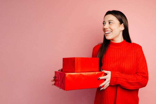 女の子はプレゼントを持っていて、彼女が受け取ったものを知りたがっています。少女は赤いセーターと黒いマニキュアを持っています - 写真・画像