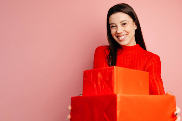 Het meisje in de rode trui met geschenken en de glimlach op haar gezicht. Meisje toont geluk en vrolijkheid - Foto, afbeelding