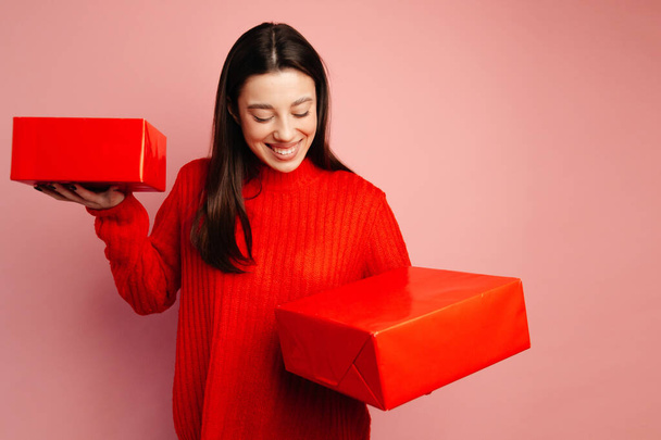 Chica en el suéter rojo y cajas de regalo rojas. La chica se ve feliz y alegre y celebrando el Día de San Valentín - Foto, imagen