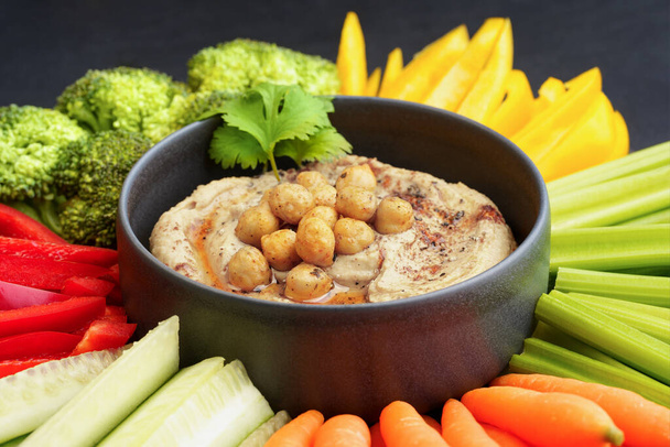 Tasty chickpeas hummus in black plate with fresh vegetables and smoked paprika - Foto, afbeelding