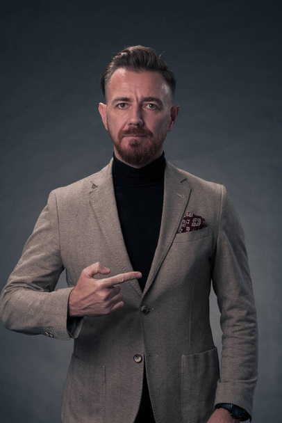 Portrait of a stylish elegant senior businessman with a beard and casual business clothes in photo studio isolated on dark background gesturing with hands. High quality photo - Zdjęcie, obraz