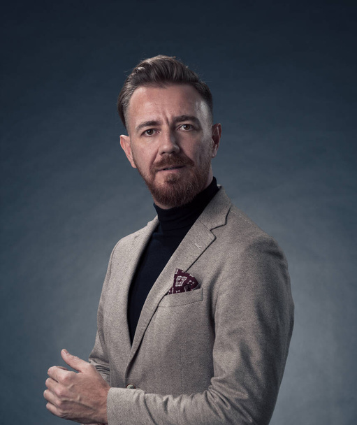 Portrait of a stylish elegant senior businessman with a beard and casual business clothes in photo studio isolated on dark background gesturing with hands. High quality photo - Photo, Image