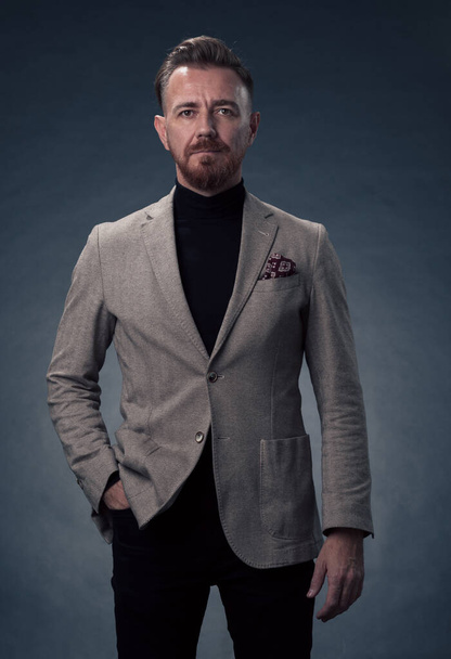 Portrait of a stylish elegant senior businessman with a beard and casual business clothes in photo studio isolated on dark background gesturing with hands. High quality photo - Foto, immagini