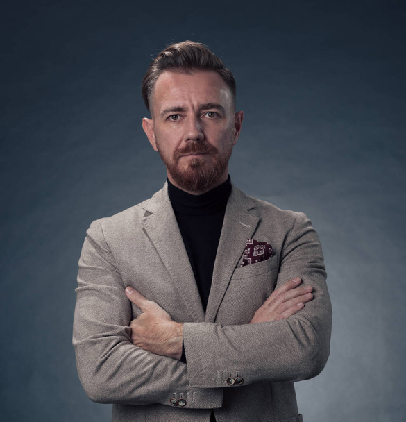 Portrait of a stylish elegant senior businessman with a beard and casual business clothes in photo studio isolated on dark background gesturing with hands. High quality photo - 写真・画像