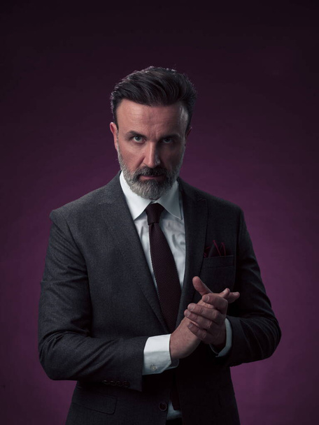 Portrait of a stylish elegant senior businessman with a beard and casual business clothes in photo studio isolated on dark background gesturing with hands. High quality photo - Фото, зображення