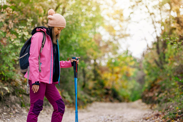 Hiker girl standing on a wide trail in the mountains. Backpacker with pink jacket in a forest. Healthy fitness lifestyle outdoors. - Fotografie, Obrázek