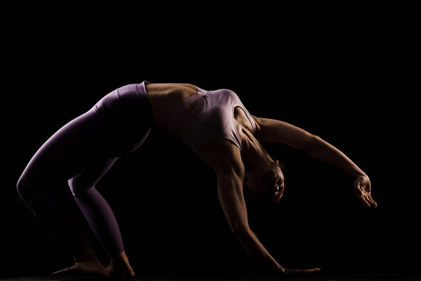 Fit girl practicing yoga in a studio. Half silhouette side lit fitness model - Fotó, kép