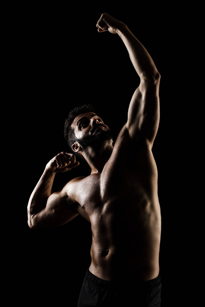 Side lit muscular Caucasian man silhouette. Athlete posing against black background.  - Photo, image