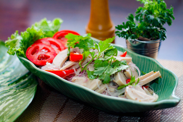 Würziger vietnamesischer Wurstsalat in einem blattförmigen grünen Teller. Mit Zwiebeln, Knoblauch, Paprika auf einem schwarzen Holztisch in Thailand. - Foto, Bild