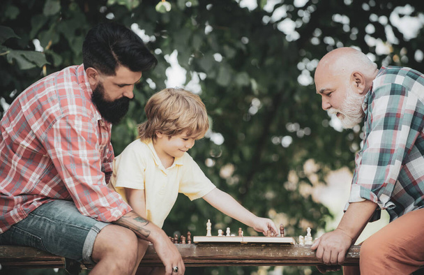 Concept of Fathers day. Senior man teaching his grandson to play chess. Happy man family concept playing Chess and have fun together. - Φωτογραφία, εικόνα