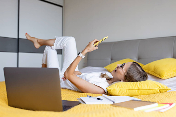 Young Woman student studying online via video chat. Stylish freelancer works from home. Blogger working from home office. Millennial business woman lying on bed in modern apartment.  - Фото, зображення
