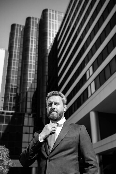 Business man in blue suit tying the necktie outdoor. Well dressed businessman on city office building. - Фото, изображение