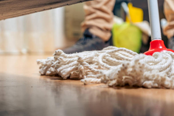 A normal view from below of an armchair of a rope mop being wiped across the floor of a house. Cleaning work. - Foto, Bild