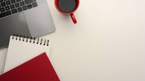 Moderner Arbeitsplatz mit Laptop, Notizblock, Kaffeetasse und Kopierraum auf weißem Hintergrund. Ansicht von oben - Foto, Bild