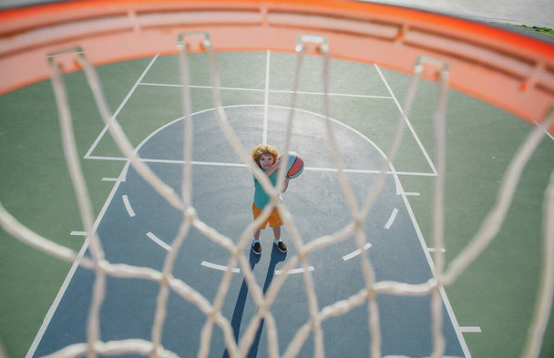 Angle view from on top of basketball basket, selective focus on basketball kid player. Sport texture background. - Foto, afbeelding