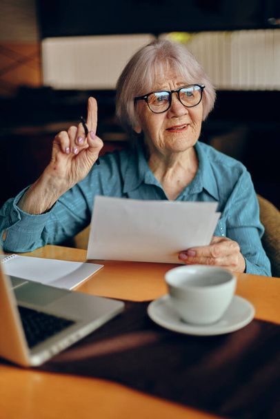 elderly woman with glasses sits at a table in front of a laptop Social networks unaltered - Foto, immagini