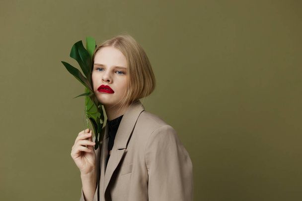 blond vrouw in jas rood lippen mode palmblad studio model ongewijzigd - Foto, afbeelding
