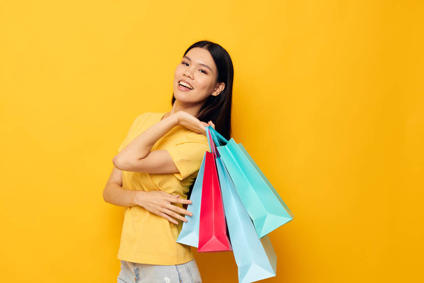 woman with Asian appearance in a yellow T-shirt with multicolored shopping bags isolated background unaltered - Foto, Imagen
