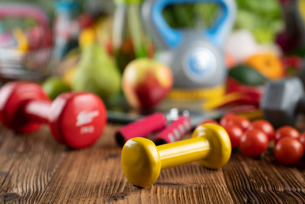 Fitness koncepció. Egészséges táplálkozás: gyümölcsök és zöldségek. Fitneszfelszerelések: súlymérő és súlyzók rusztikus faasztalon. - Fotó, kép
