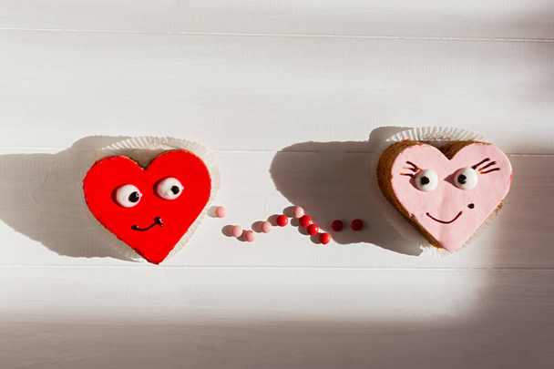 Harten taarten zijn rood en roze. Conceptuele liefde. Zoete gebakjes met lachende gezichten. Valentijnsdag, trouwdag, liefdesverklaring. Romantische stemming van zoet eten. Ontwerper oplossing voor liefhebbers - Foto, afbeelding