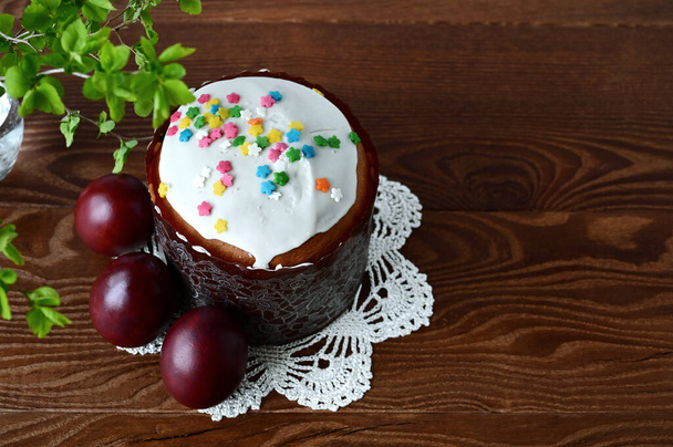 Traditional Easter cake with decorative glaze. Orthodox food after fasting on the Easter holiday. Red-painted chicken eggs on a white knitted tablecloth on a wooden table - Fotoğraf, Görsel