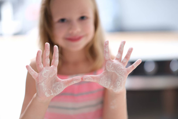 Little joyful girl shows palms in flour, close-up, blurry - Photo, Image