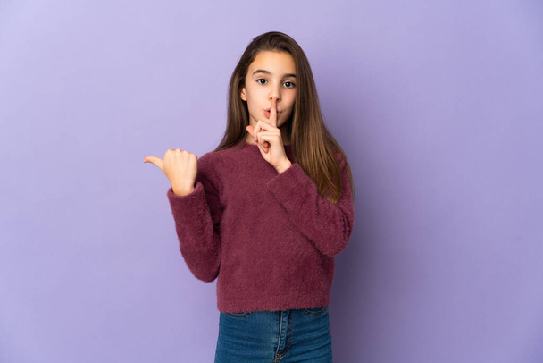 Little girl isolated on purple background pointing to the side and doing silence gesture - Photo, image