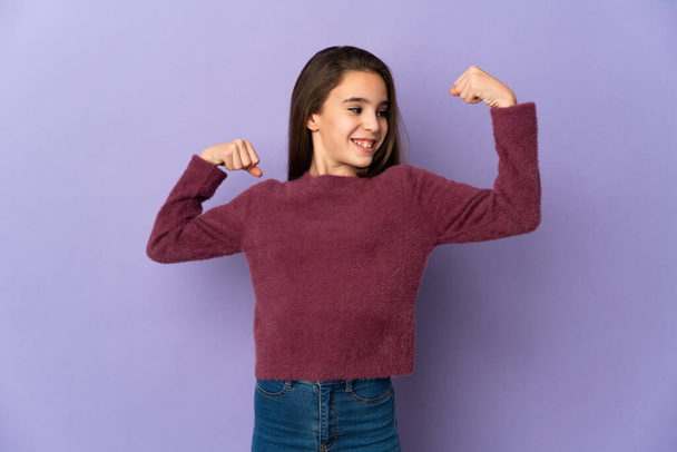 klein meisje geïsoleerd op paarse achtergrond doen sterke gebaar - Foto, afbeelding