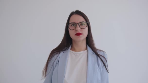 Σοβαρή νεαρή επιχειρηματίας στέκεται σε λευκό φόντο και κλείνει τα μάτια της με δυσαρέσκεια. Η έννοια των ανθρώπινων συναισθημάτων - Πλάνα, βίντεο