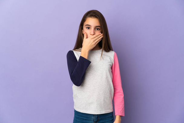 Kleines Mädchen isoliert auf violettem Hintergrund, der Mund mit der Hand bedeckt - Foto, Bild