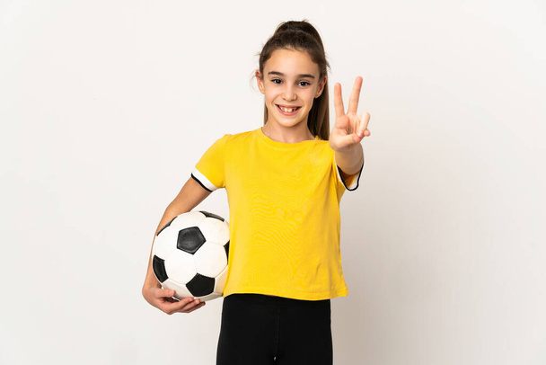 Маленькая девочка футболист изолирован на белом фоне улыбаясь и показывая знак победы - Фото, изображение