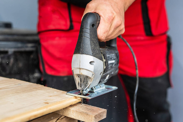 Close up on hand of unknown carpenter working with an electric jigsaw cutting wood with saw woodworking hobby concept - Photo, image