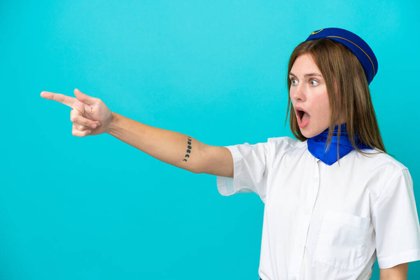 hôtesse de l'air femme anglaise isolée sur fond bleu pointant du doigt - Photo, image