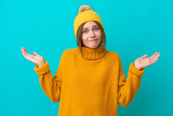 Young English woman wearing winter jacket isolated on blue background having doubts while raising hands - Photo, Image