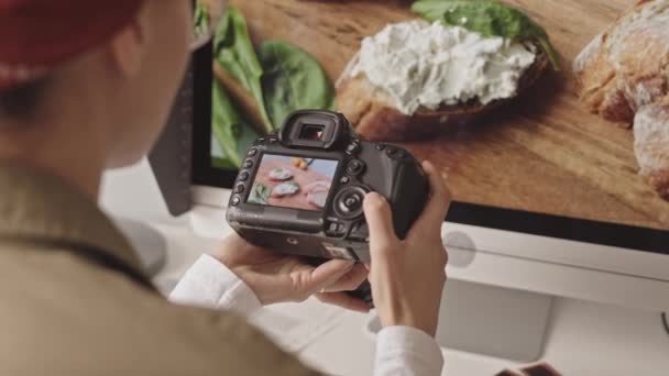 Over-the-shoulder shot of female photographer scrolling food photos on camera while working in studio - Filmagem, Vídeo