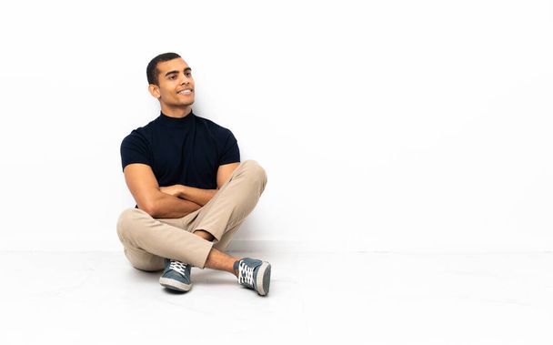 African American man sitting on the floor with arms crossed and happy - Photo, Image