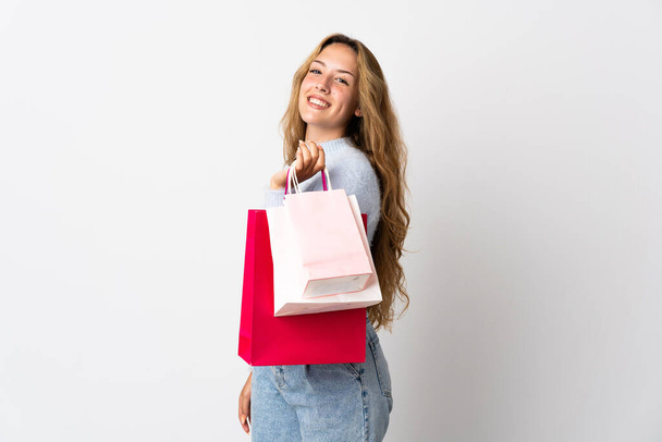Jonge blonde vrouw geïsoleerd op witte achtergrond met winkeltassen en glimlachen - Foto, afbeelding