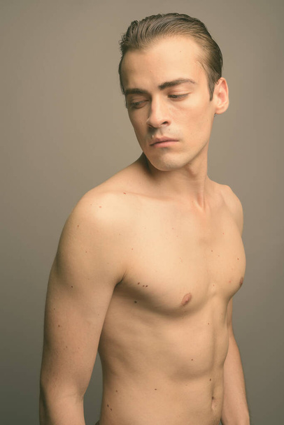 Studioaufnahme eines jungen gutaussehenden Mannes ohne Hemd vor grauem Hintergrund - Foto, Bild