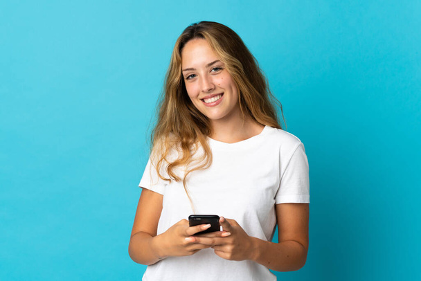 Young blonde woman isolated on blue background sending a message with the mobile - Фото, изображение