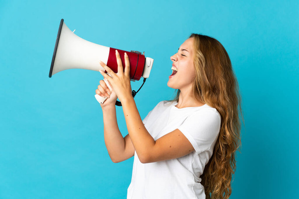 Young blonde woman isolated on blue background shouting through a megaphone - Fotografie, Obrázek