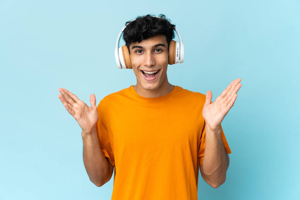 Young Argentinian man isolated on background surprised and listening music - Foto, imagen