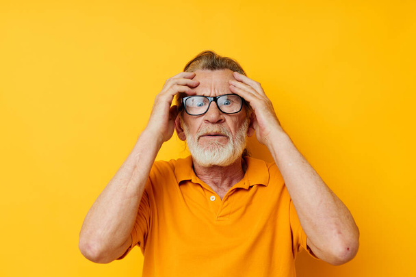 Senior grey-haired man posing yellow tshirt glasses yellow background - Zdjęcie, obraz