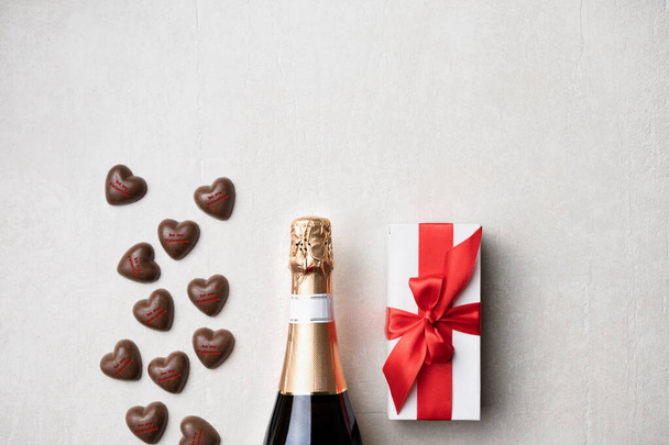 Champagne and chocolate hearts with a gift in a white box with a red bow on a light background with copy space - Photo, Image