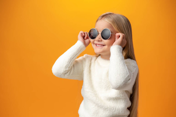 Sarı arka planda güneş gözlüğü takan küçük bir kız. - Fotoğraf, Görsel