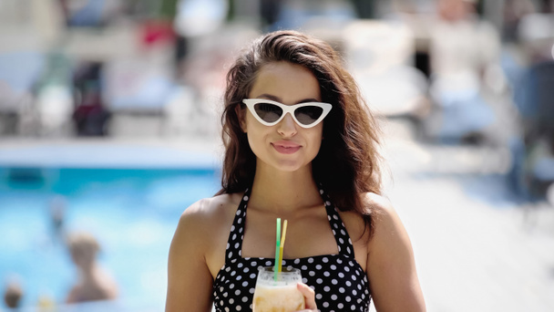 счастливая молодая женщина в солнечных очках и купальнике, держа коктейль в стакане - Фото, изображение