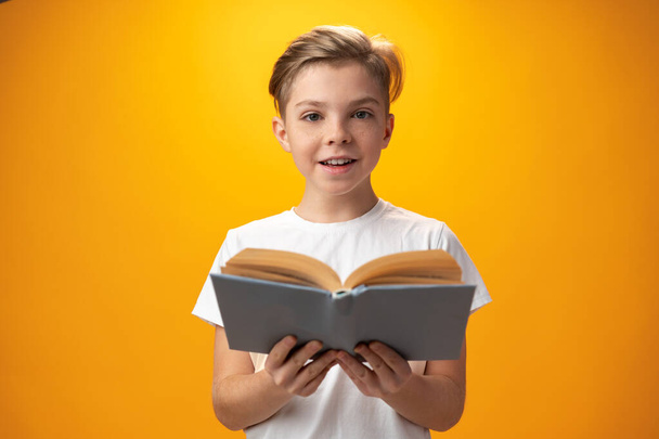 Little schoolboy holding a book against yellow background - Foto, Imagem